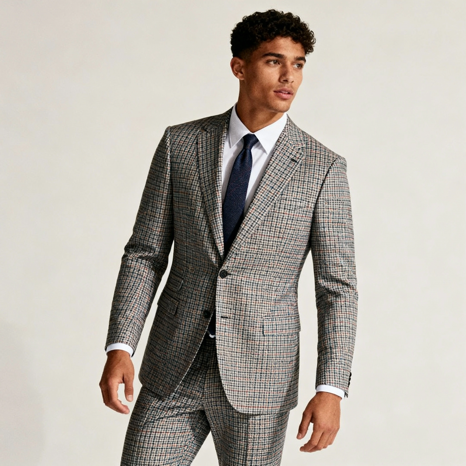 Man wearing a gray checkered suit with a white shirt and dark tie on a plain background